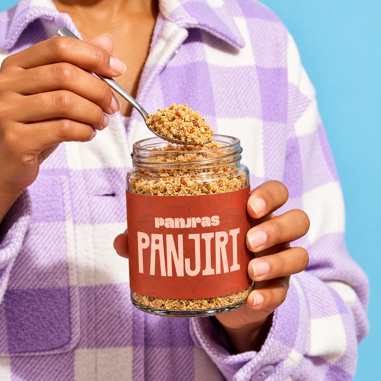 A spoonful of panjiri being scooped from an open PanjRas jar